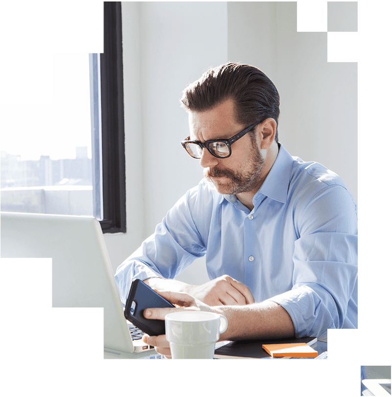 Man looking at laptop while holding phone next to coffee