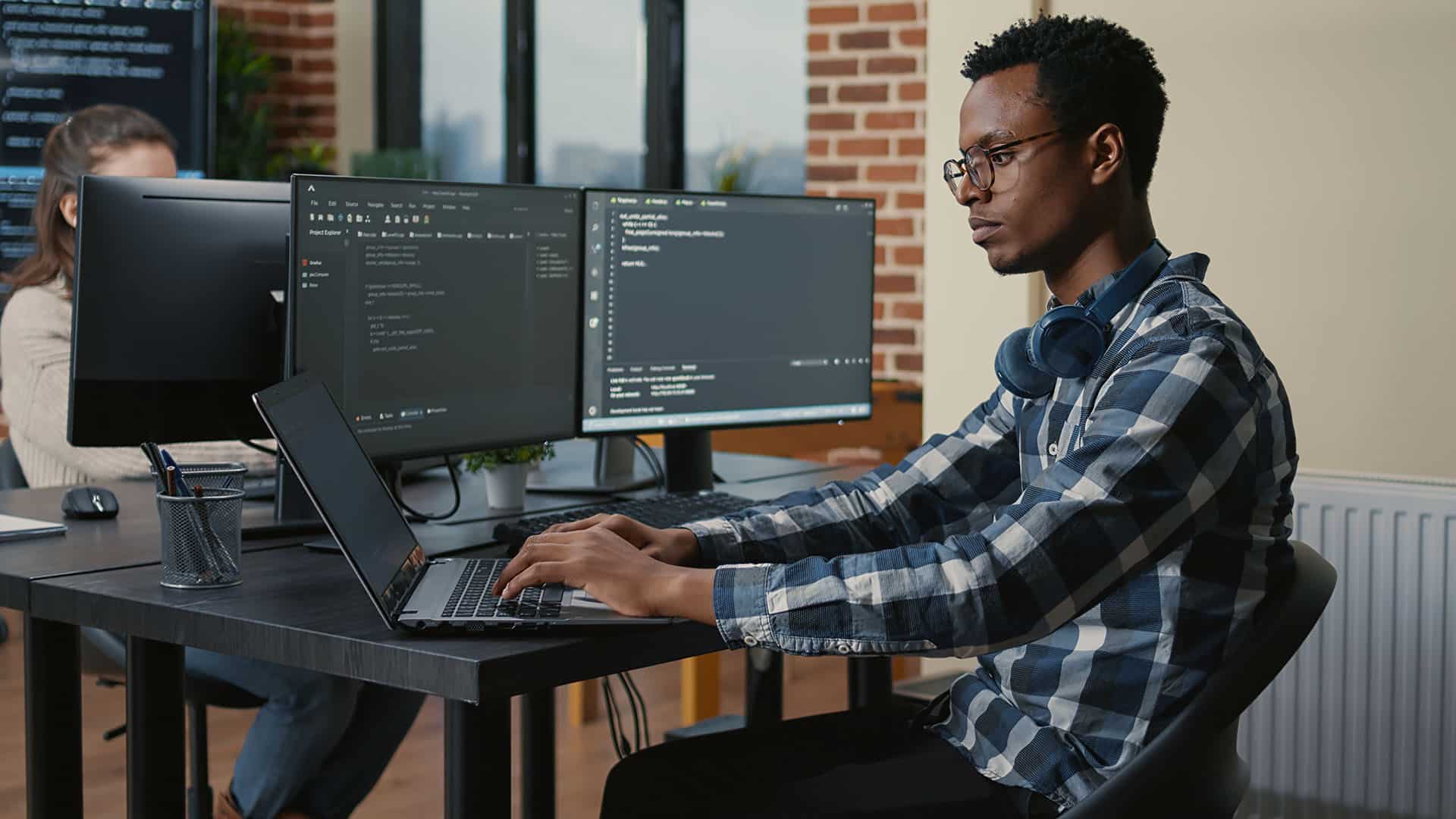 Programer working on laptop while coding on desktop monitors
